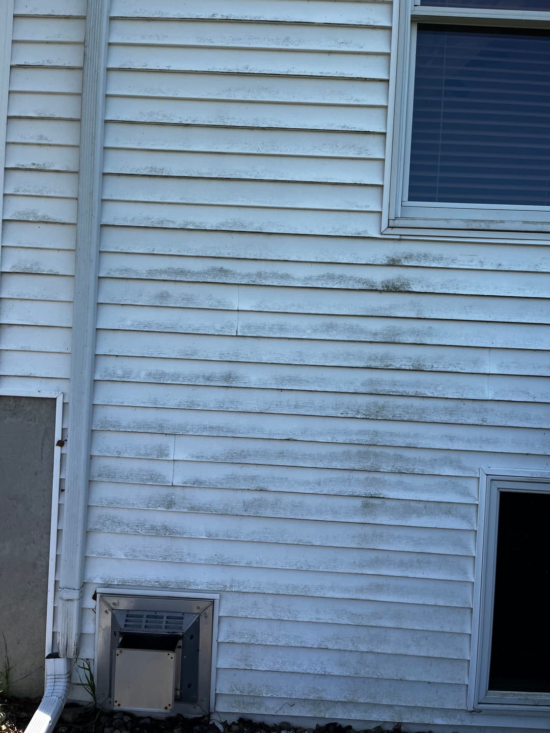 Dirty white vinyl siding with stains, air conditioning unit, and nearby window.