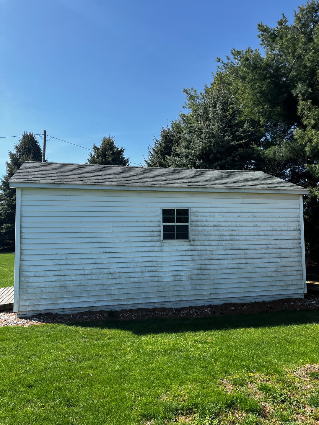 Side view of a weathered white shed with a small window and green grass foreground.