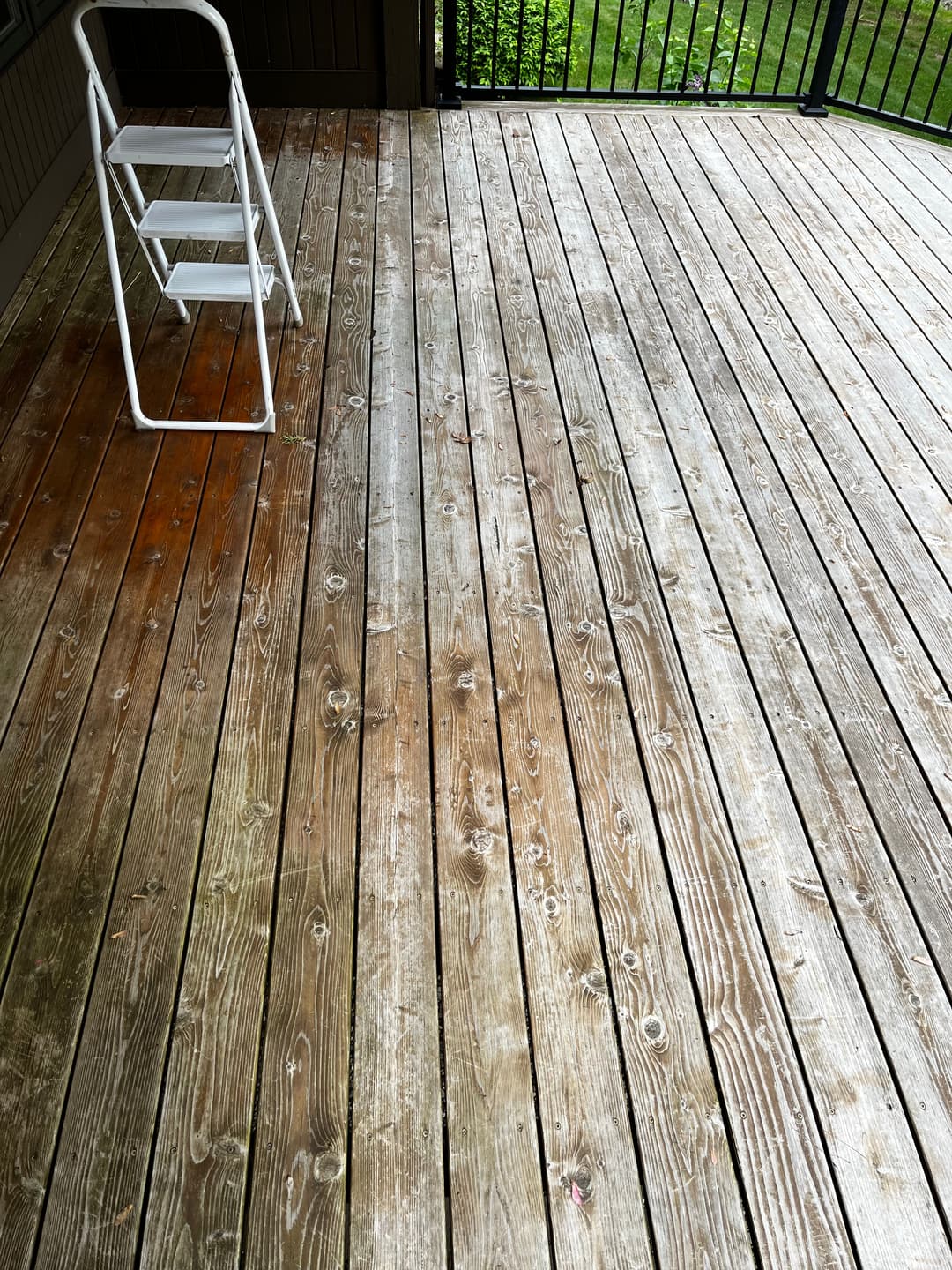 Weathered wooden deck with a white folding ladder, surrounded by greenery.