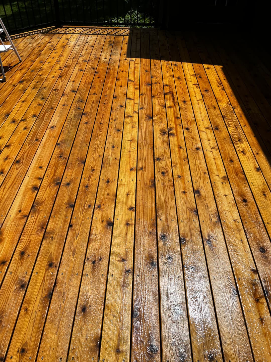 Shiny wooden deck with natural grain, illuminated by sunlight and shadow.