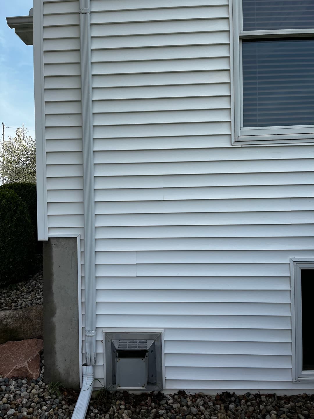 White house exterior with siding and a vent near the foundation, surrounded by gravel.