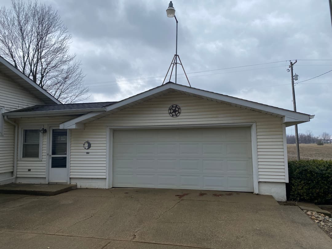 Front view of a house with a garage door, light fixture, and cloudy sky backdrop.