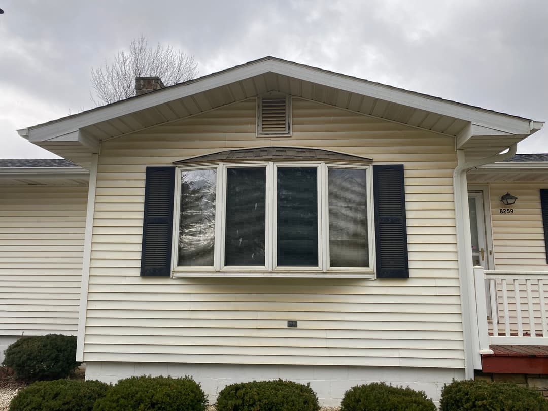 Front view of a beige house with a decorative bay window and dark shutters.