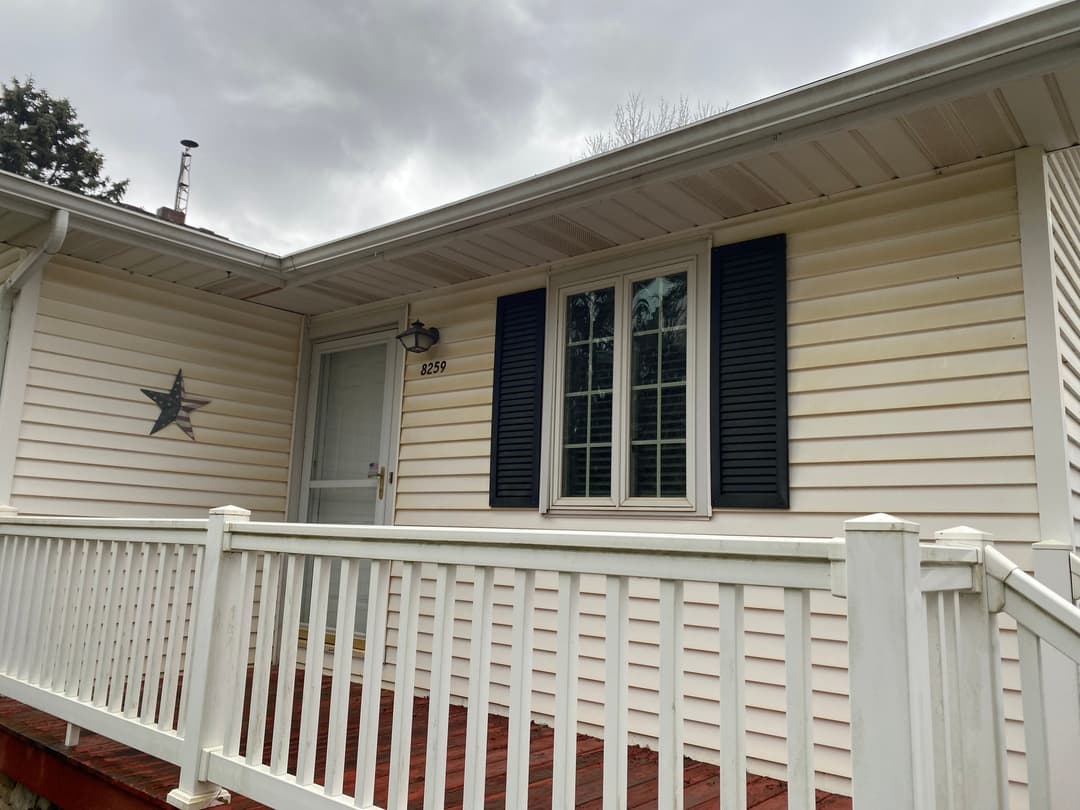 Front view of a white house with black shutters and a wooden porch railing.