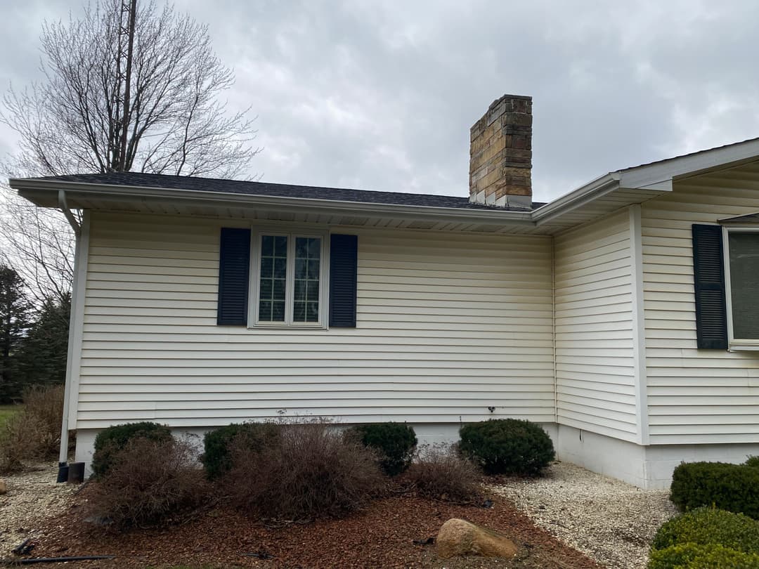 Side view of a single-story house with a stone chimney and landscaped yard.