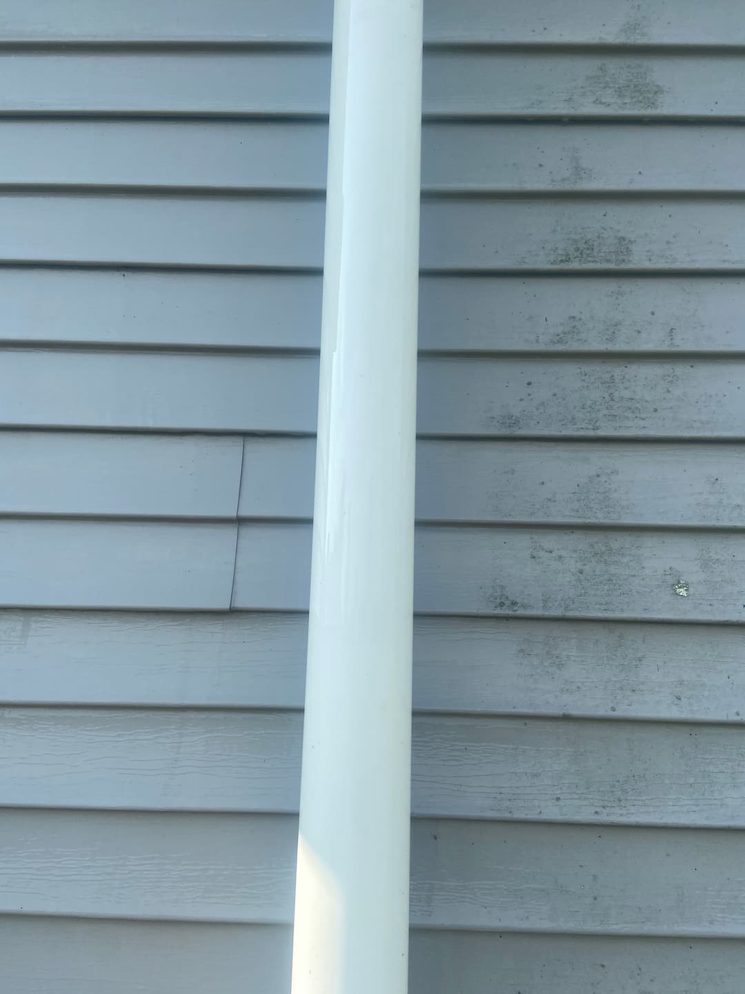 White vertical pipe against gray wooden siding with visible texture and wear.