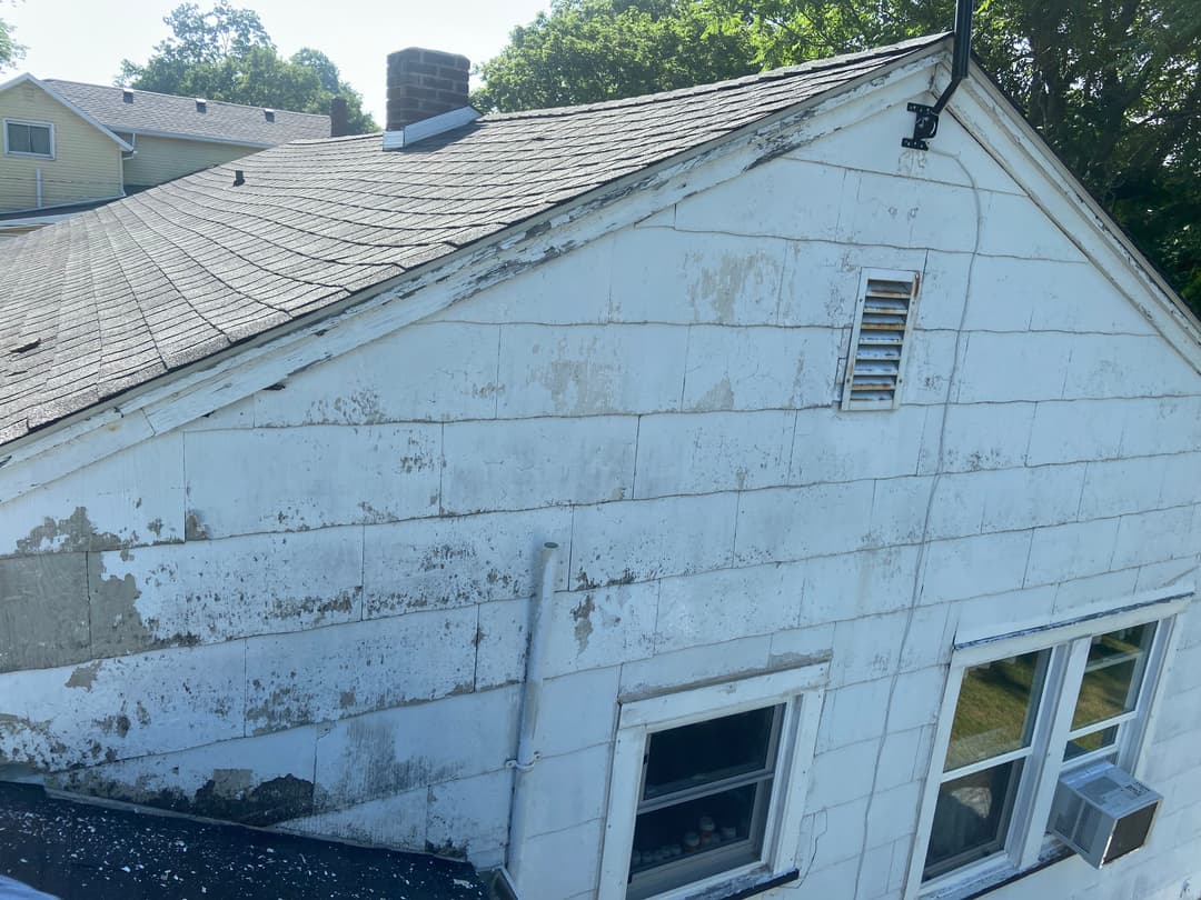 Weathered house exterior with peeling paint, old shingles, and ventilation panel on roof.