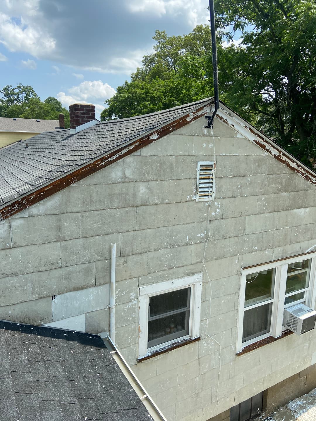 Old house exterior with peeling paint, showcasing roof and window details under cloudy sky.