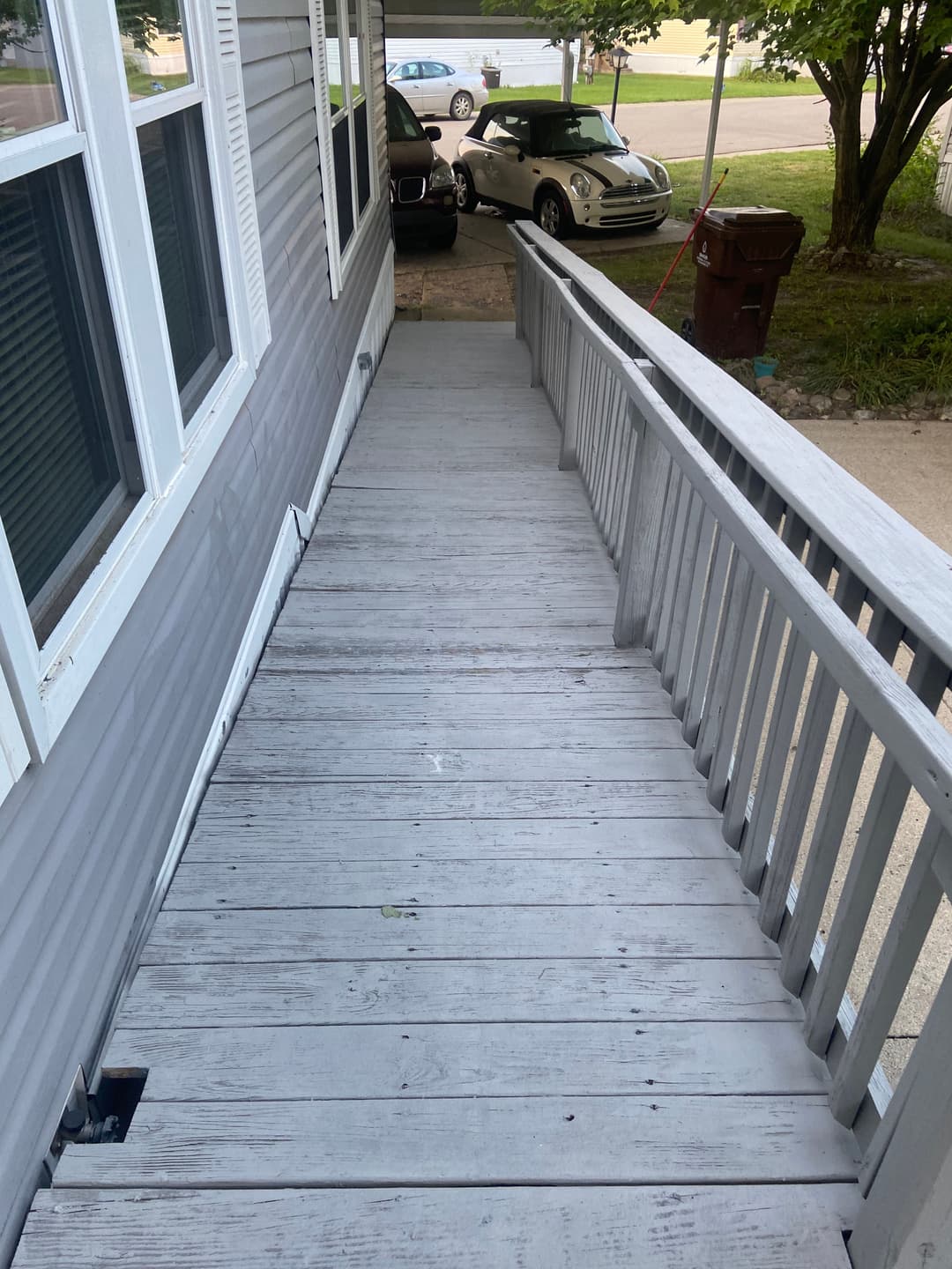 Gray wooden ramp leading to a house with parked cars nearby, showcasing accessible design.