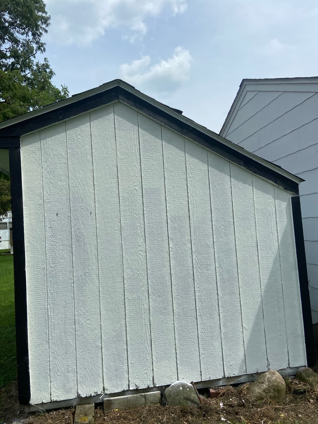 Side view of a white wooden shed with a black trim and a slanted roof.