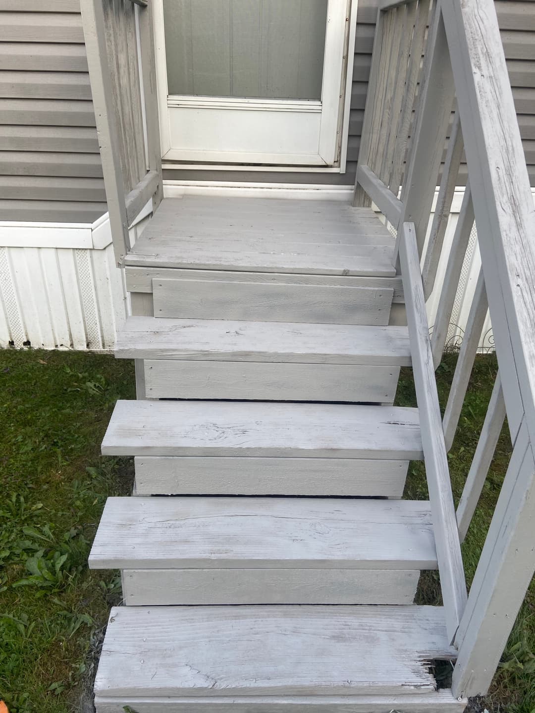 Gray wooden stairs leading to a door with a white railing and grassy area.
