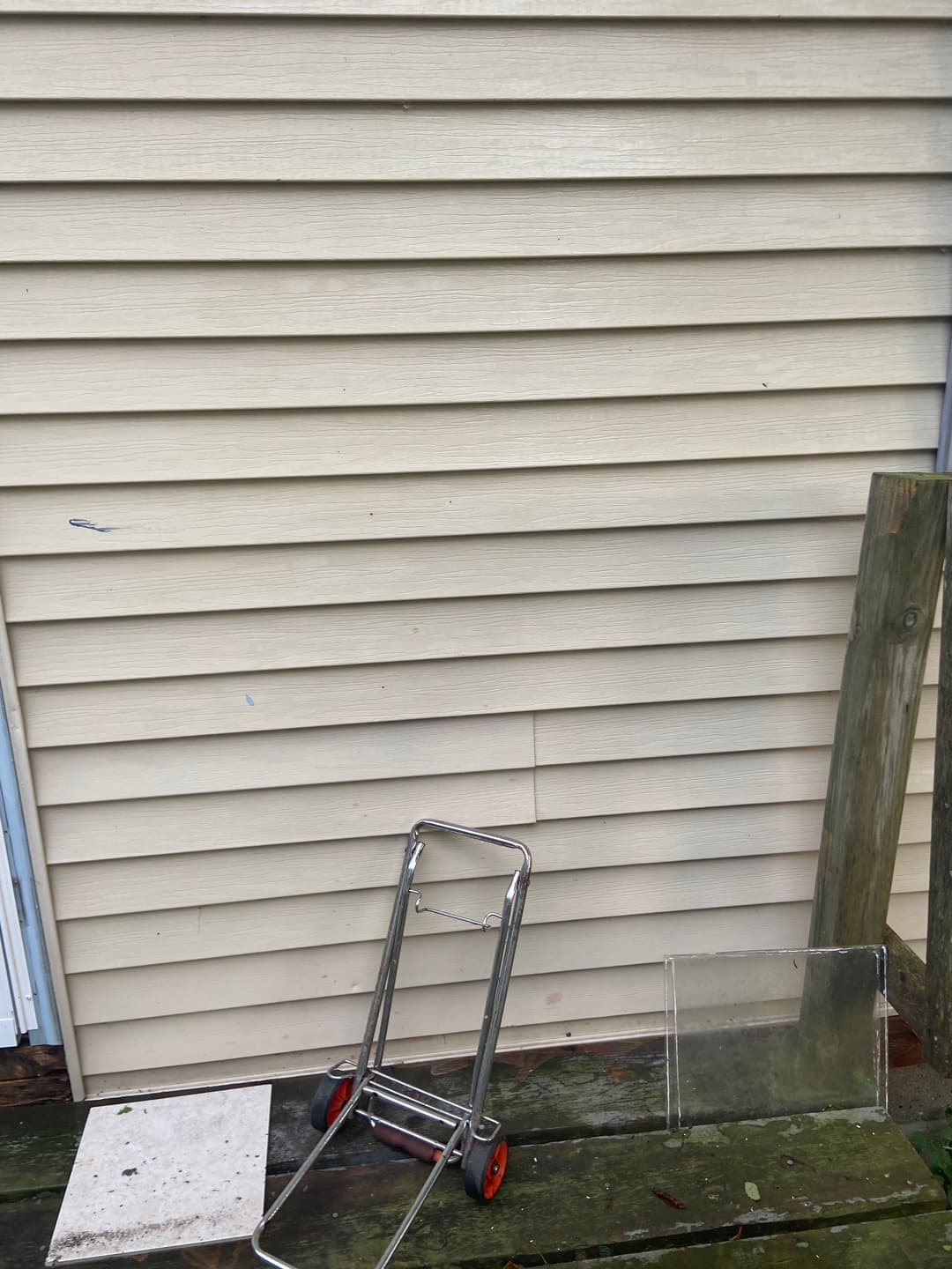 Metal cart, clear plastic sheet, wooden plank, and tile on a wooden surface by a beige wall.