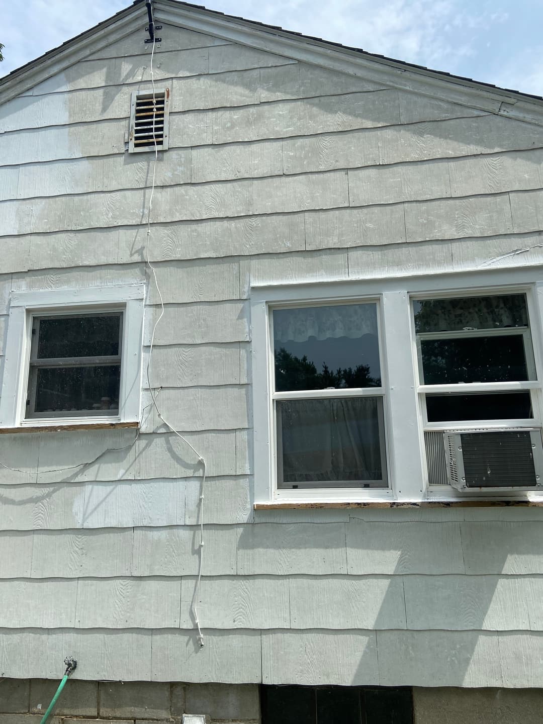 Exterior shot of a light-colored house with windows and an air conditioning unit.