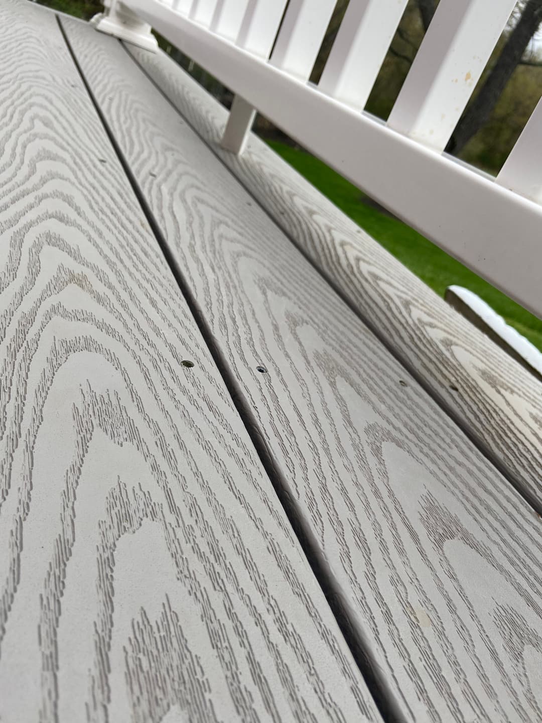 Close-up of gray wooden deck planks with a white railing in the background.