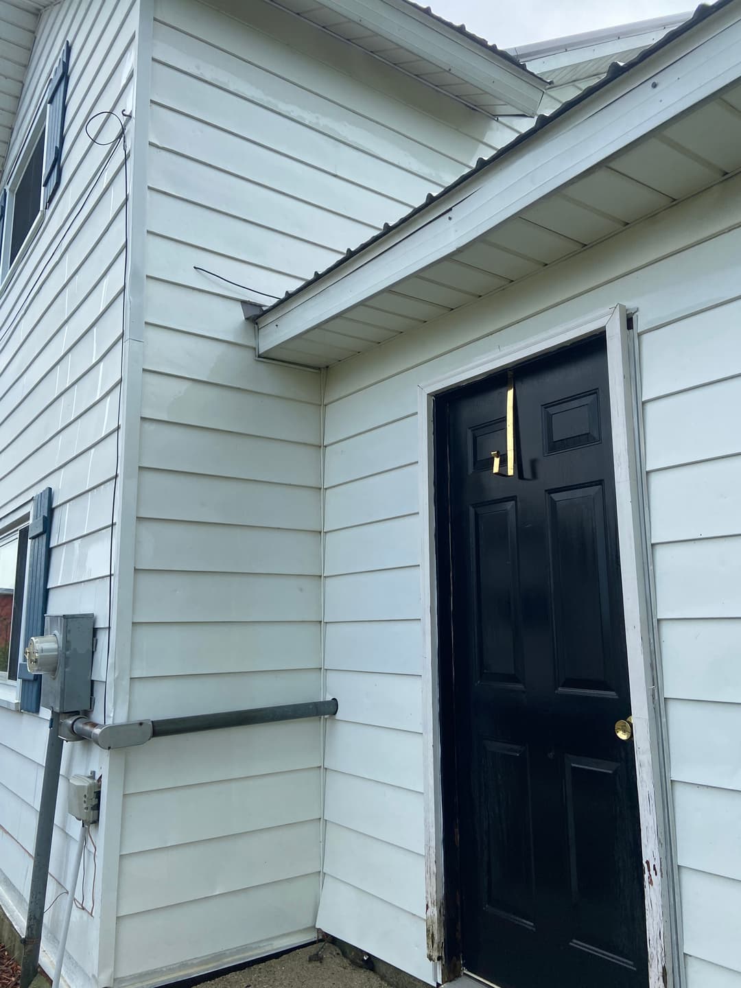 Black door on a white house exterior with adjacent electrical meter and corner detail.