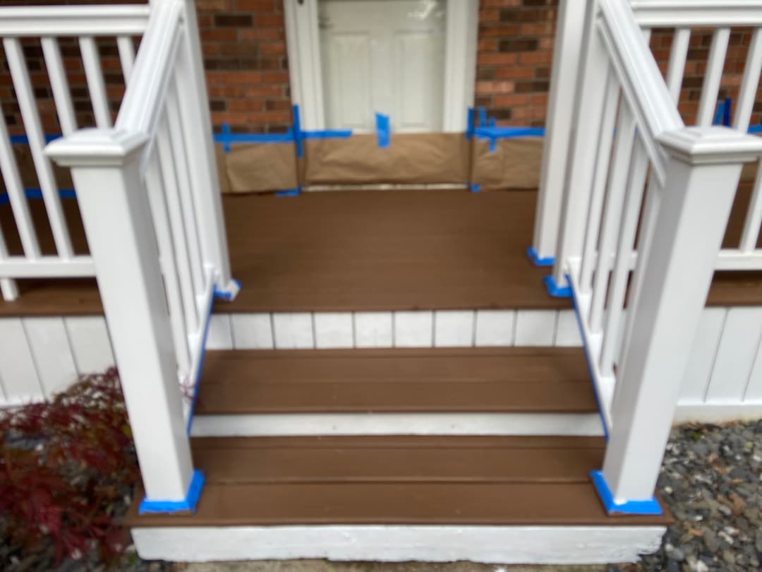 Freshly painted brown porch steps with blue painter's tape, landing, and white railings.