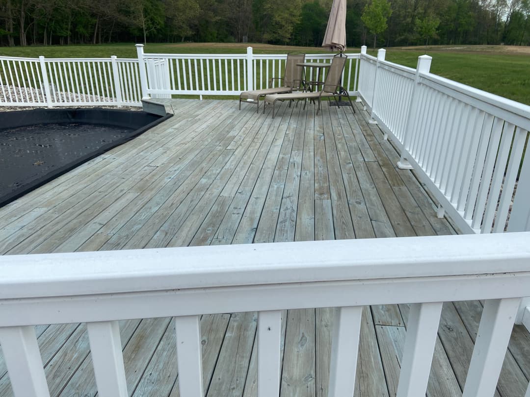 Wooden deck with white railing and lounge chair overlooking grassy area.
