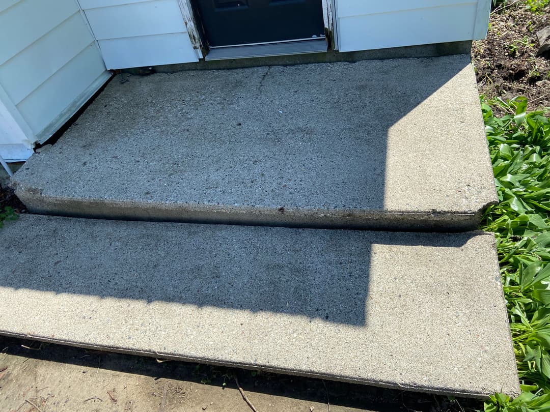 Concrete steps leading to a door, with sunlight casting shadows on the surface.