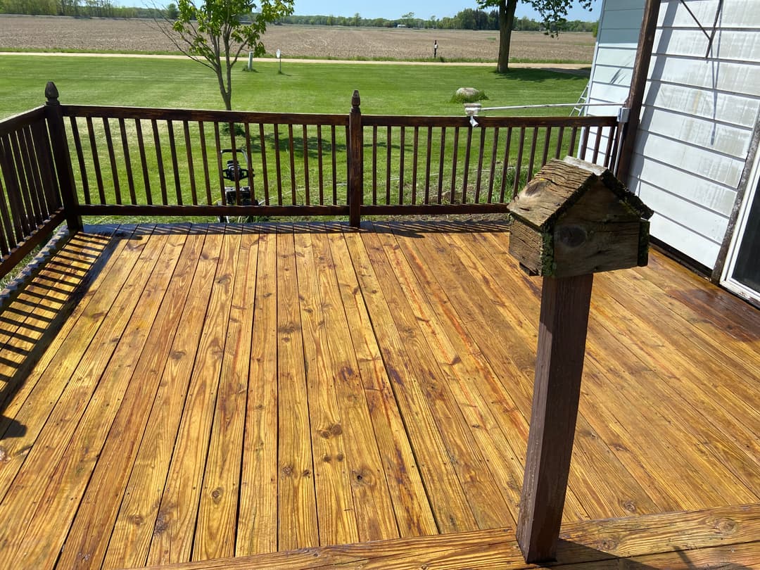 Wooden deck with railing, birdhouse, and lush green field in the background.