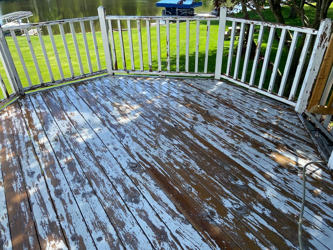 Weathered wooden deck with peeling white paint overlooking a serene lake.