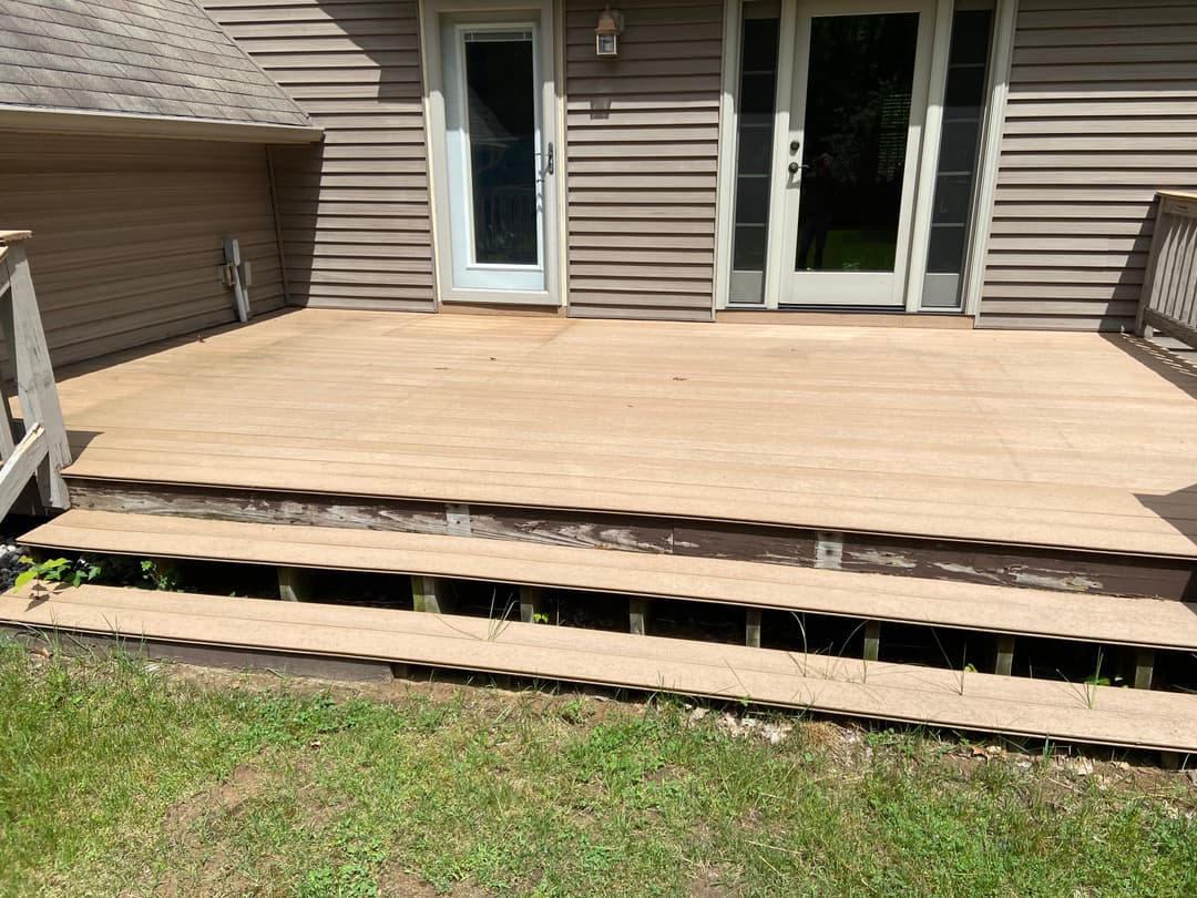 Newly constructed wooden deck with steps and green grass, enhancing outdoor living space.