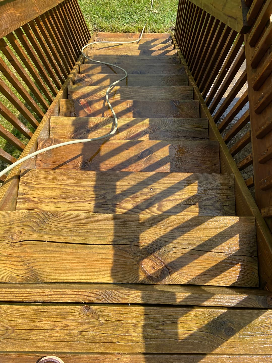 Wooden staircase descending with sunlight casting shadows and garden view at the bottom.