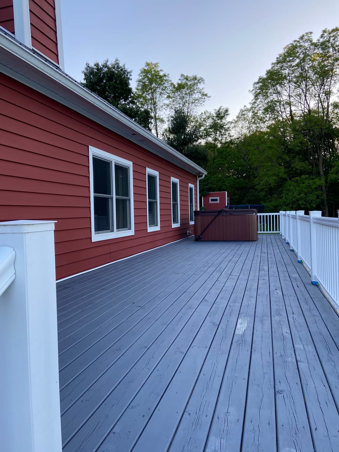 Red house exterior with gray deck and white railing surrounded by green trees.