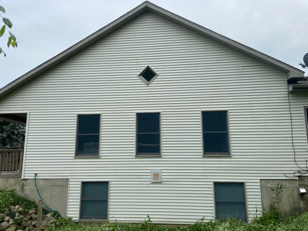 Side view of a residential home with white siding, dark windows, and a decorative diamond window.
