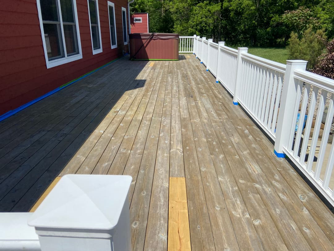 Spacious wooden deck with white railing and green trees in the background, freshly stained.