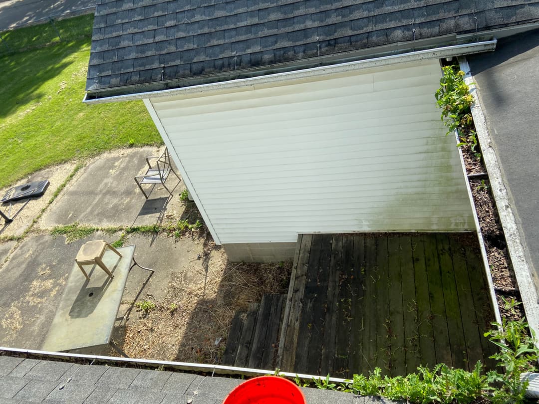 Aerial view of a house corner showing a wooden deck and overgrown vegetation.