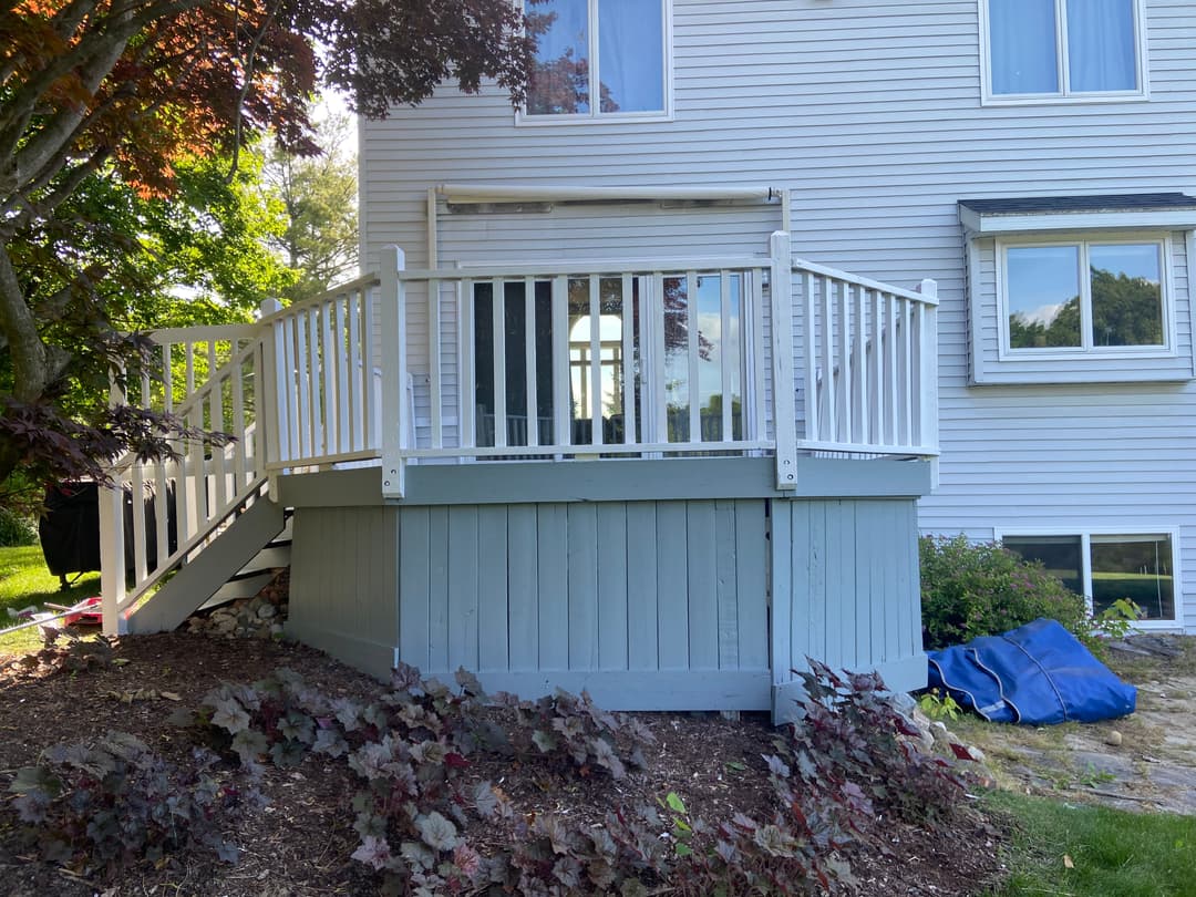 Exterior view of a home with a white deck and stairs, surrounded by greenery and landscaping.