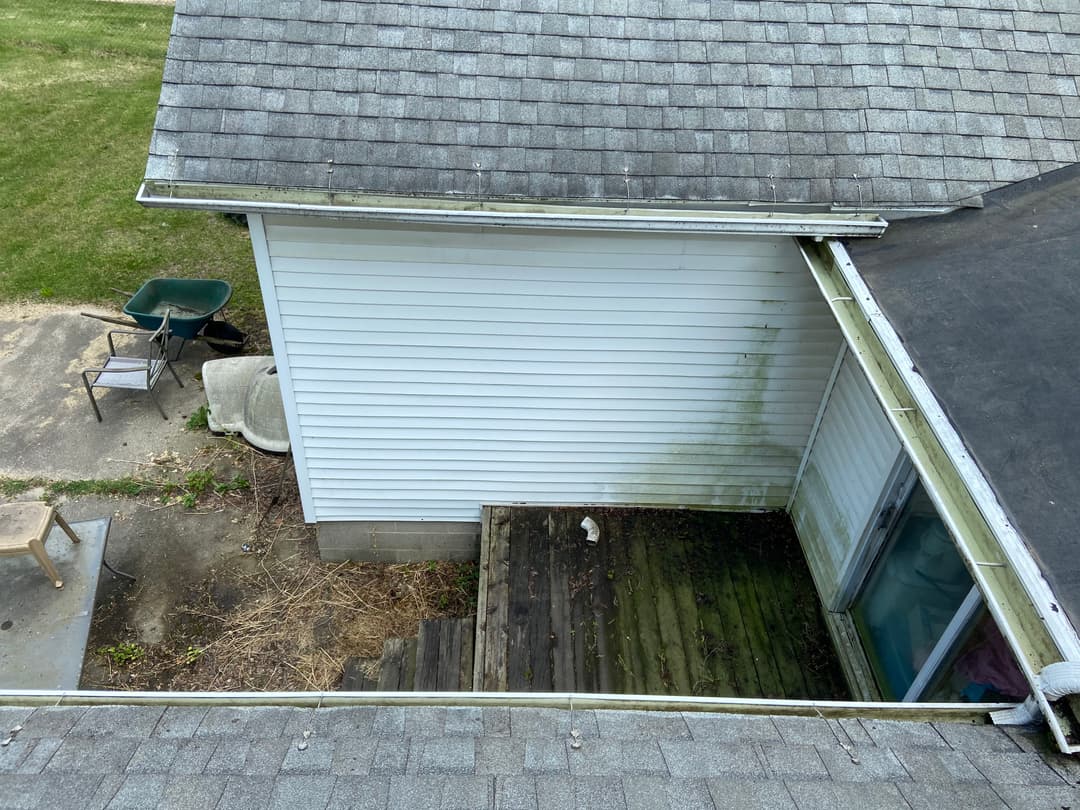 Aerial view of a home's roof, adjacent white siding, and overgrown wooden deck area.
