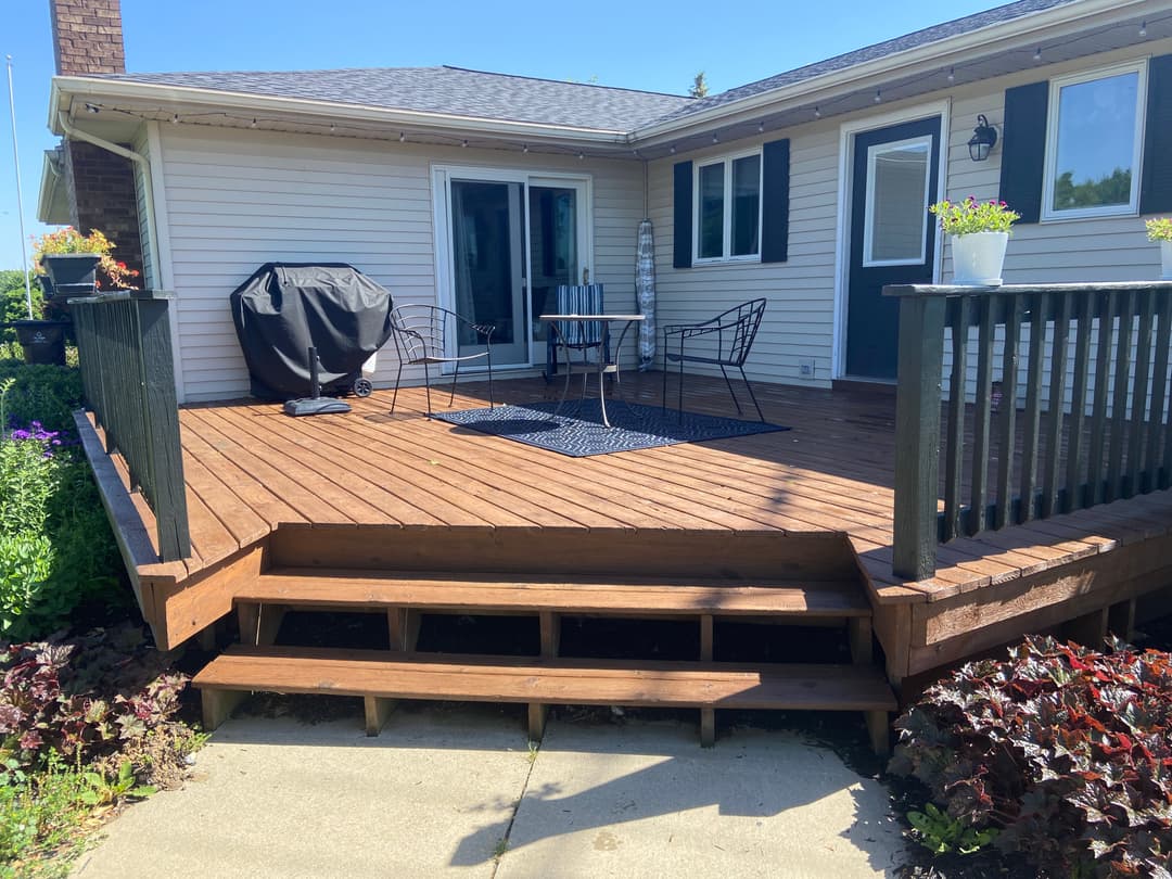 Cozy wooden deck with outdoor seating and grill, surrounded by vibrant flowers.