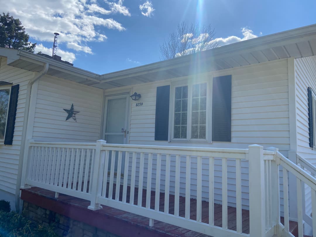 Front view of a cozy white house with a porch and star decoration, under a sunny sky.