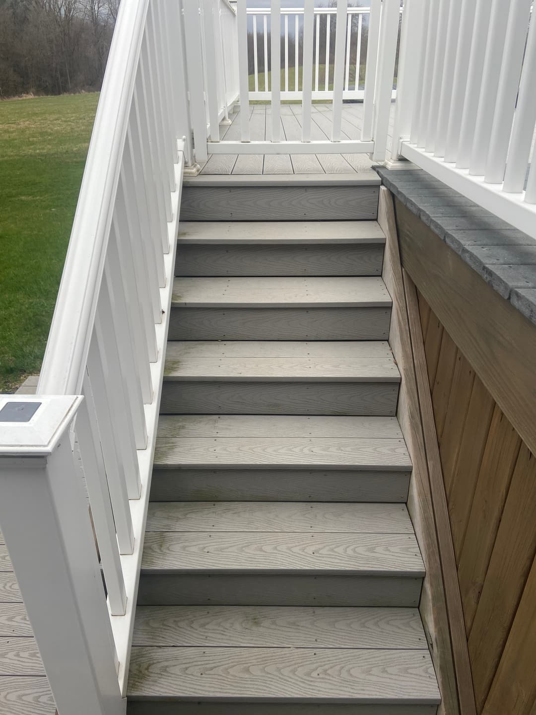 Sturdy wooden stairs leading to a balcony with white railing and green lawn view.