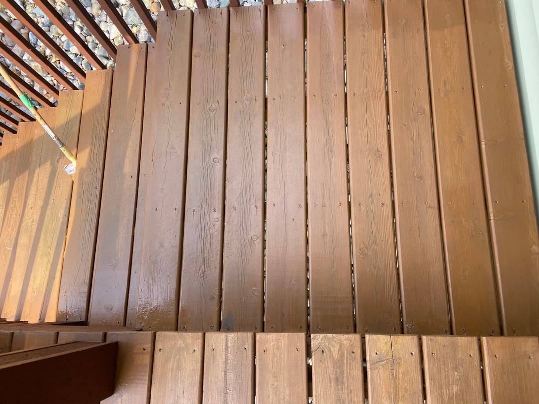 Newly painted brown wooden deck with clean, straight planks and sunlight casting shadows.