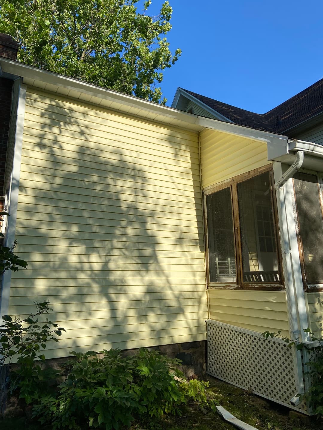 Yellow house exterior with shadowed trees, showcasing siding and screened porch area.