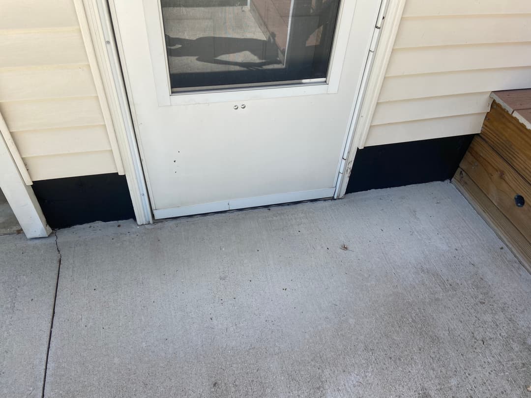 White door with a concrete step leading to a patio, featuring a black painted trim.