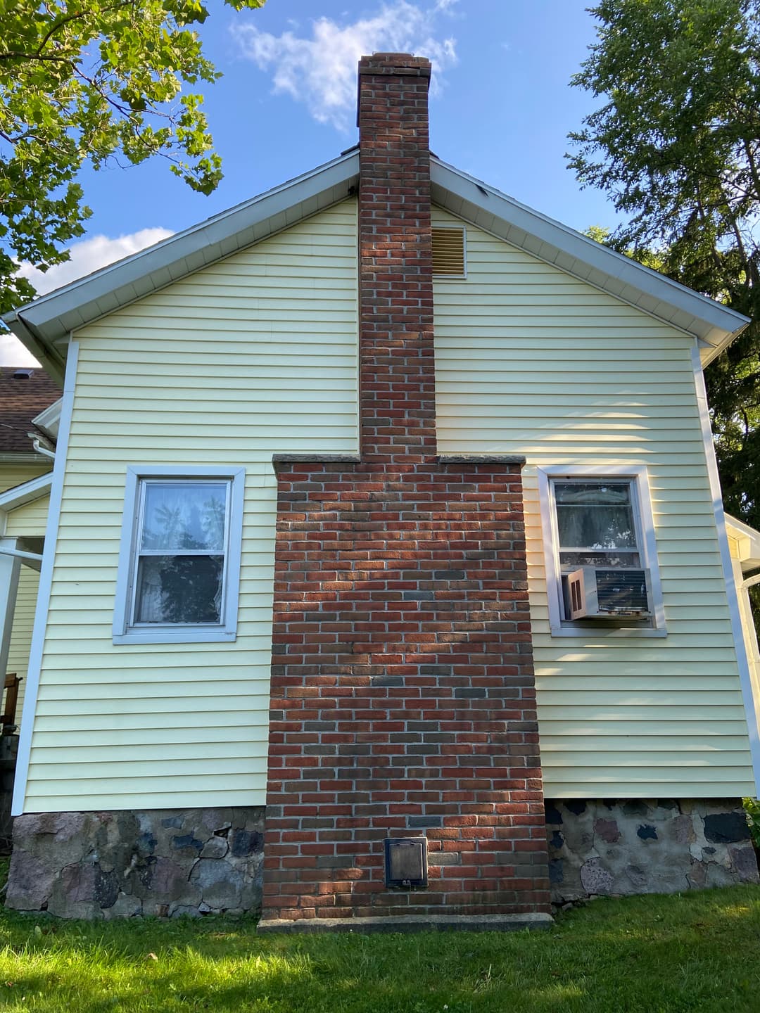 Yellow house with brick chimney and window air conditioner on the exterior wall.