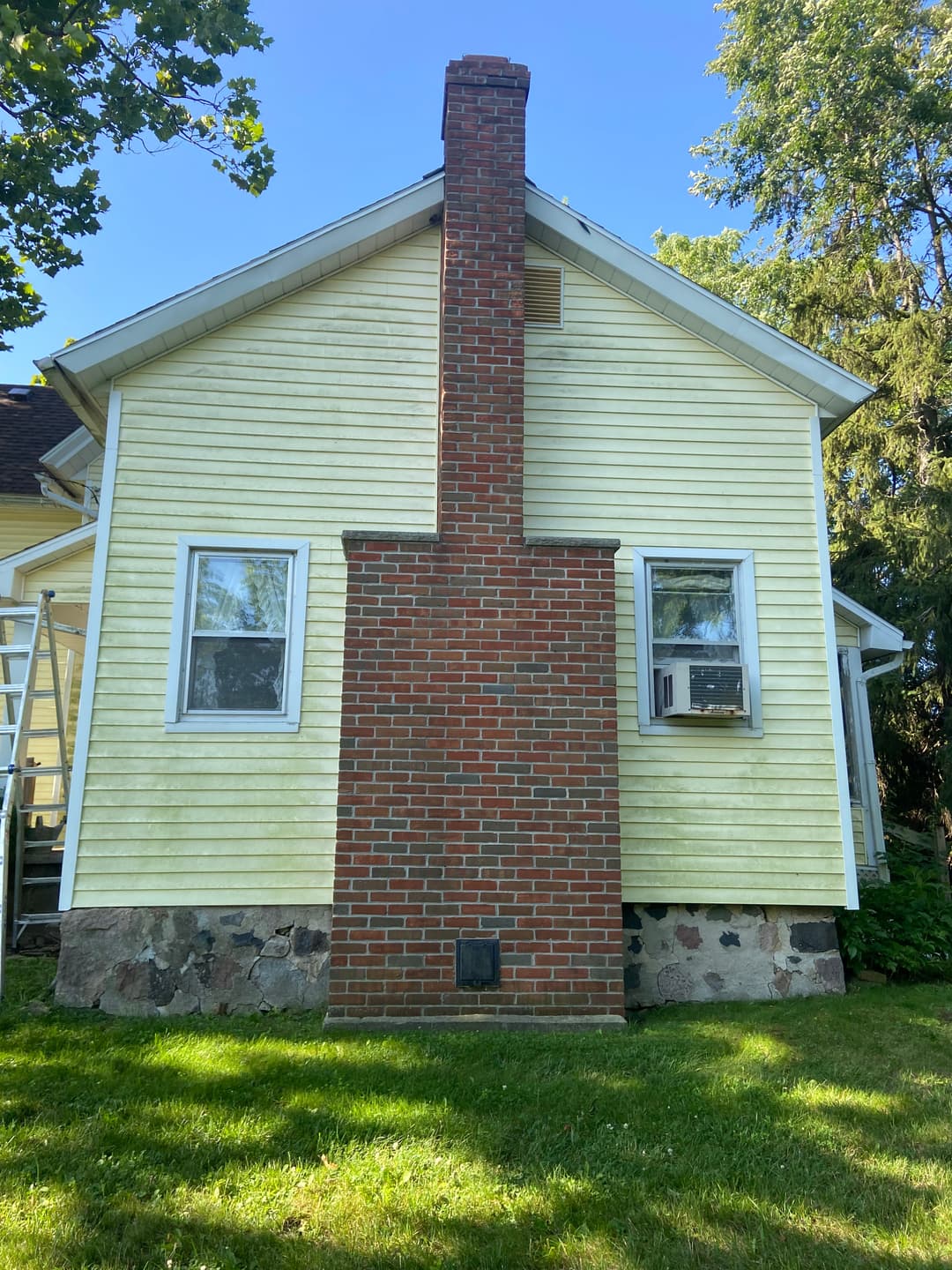 Yellow house exterior with a brick chimney, two windows, and air conditioner unit visible.