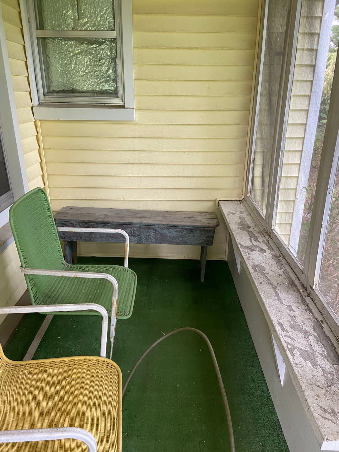 Porch with green and yellow chairs, wooden bench, and sunlight streaming through windows.