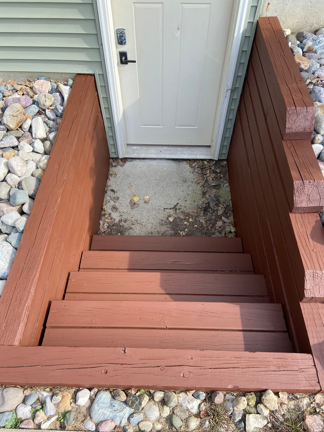 Wooden steps leading to a door surrounded by gravel and green siding.