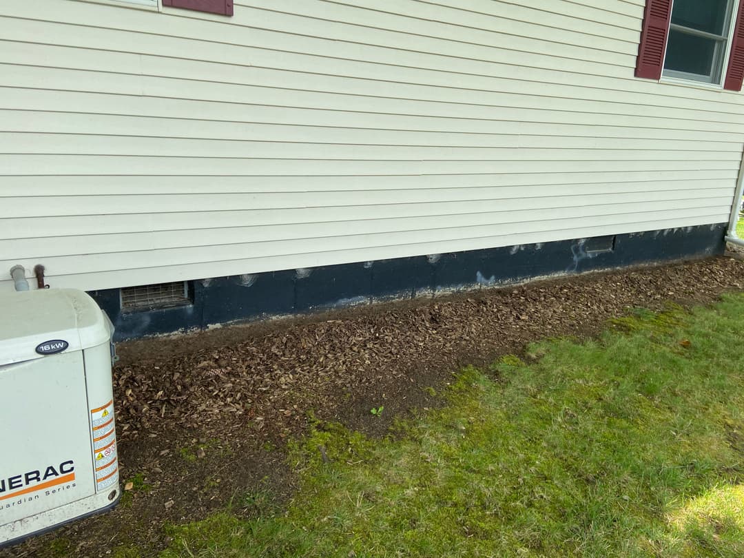 Side view of a house exterior showing foundation, fresh mulch, and an electrical unit.