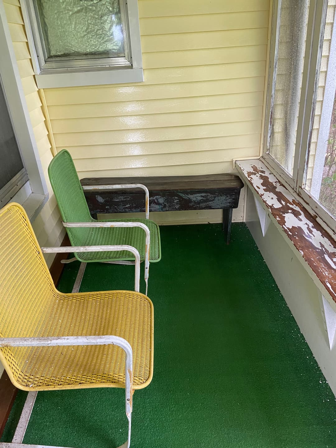 Vintage porch with yellow and green chairs on green carpet and a weathered wooden bench.