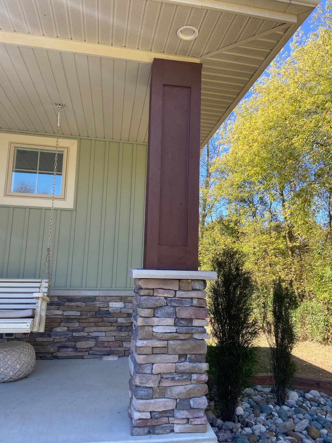 Modern home entrance featuring a stone pillar and wooden column with a porch swing.