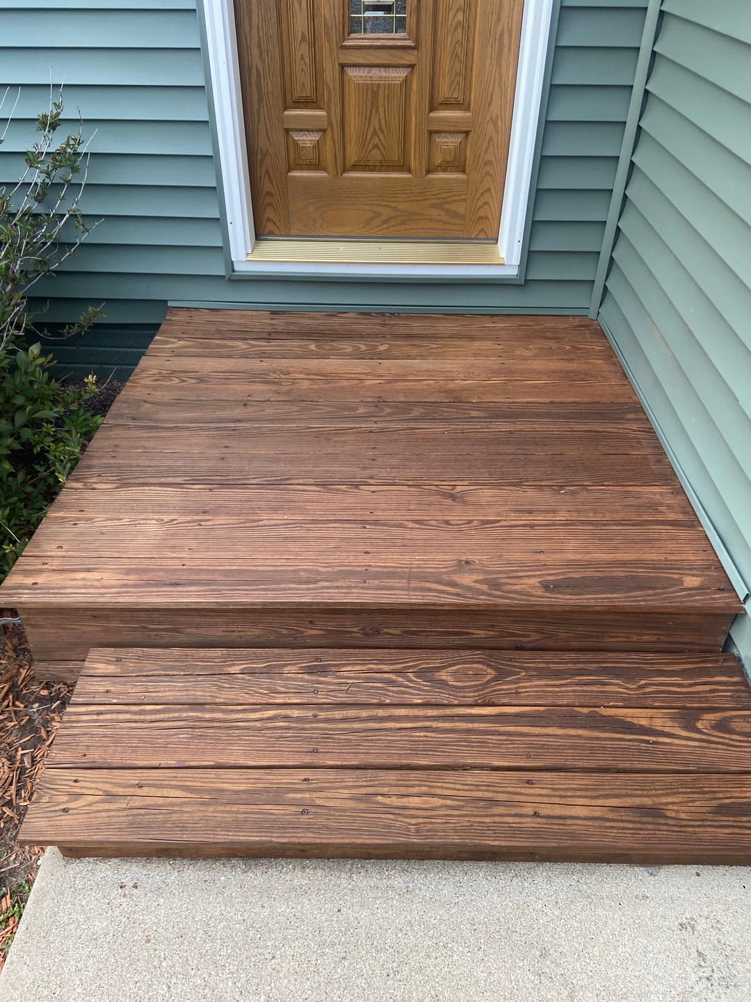 Wooden porch steps leading to a front door, showcasing a rich brown finish and well-maintained surface.