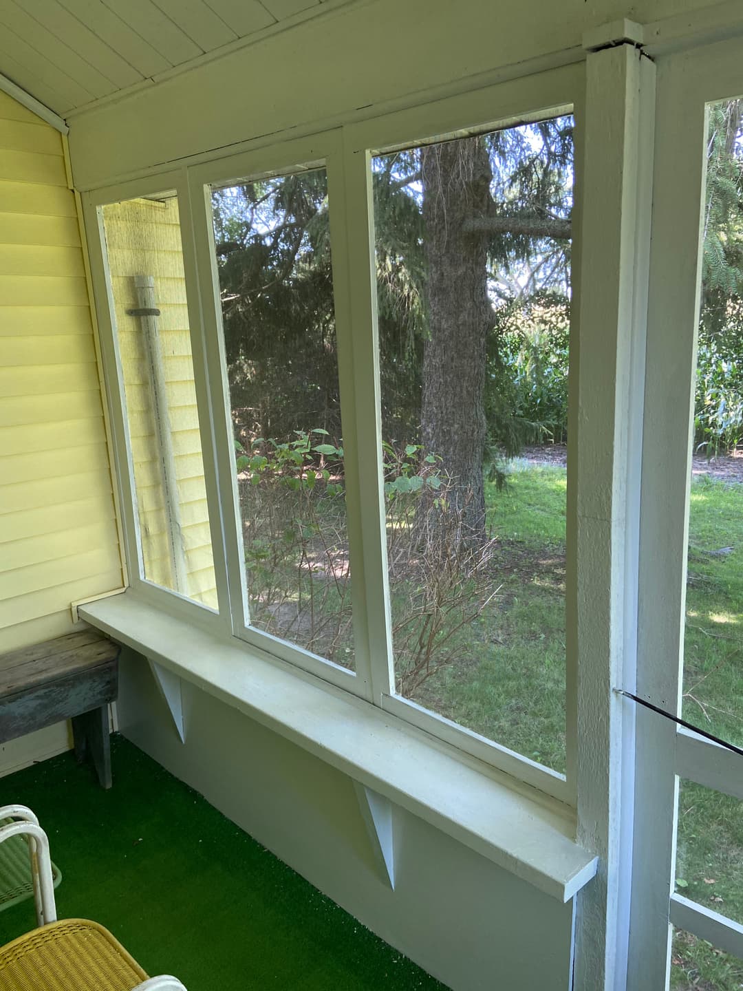 Cozy screened porch with green carpet and sunlight filtering through large windows.