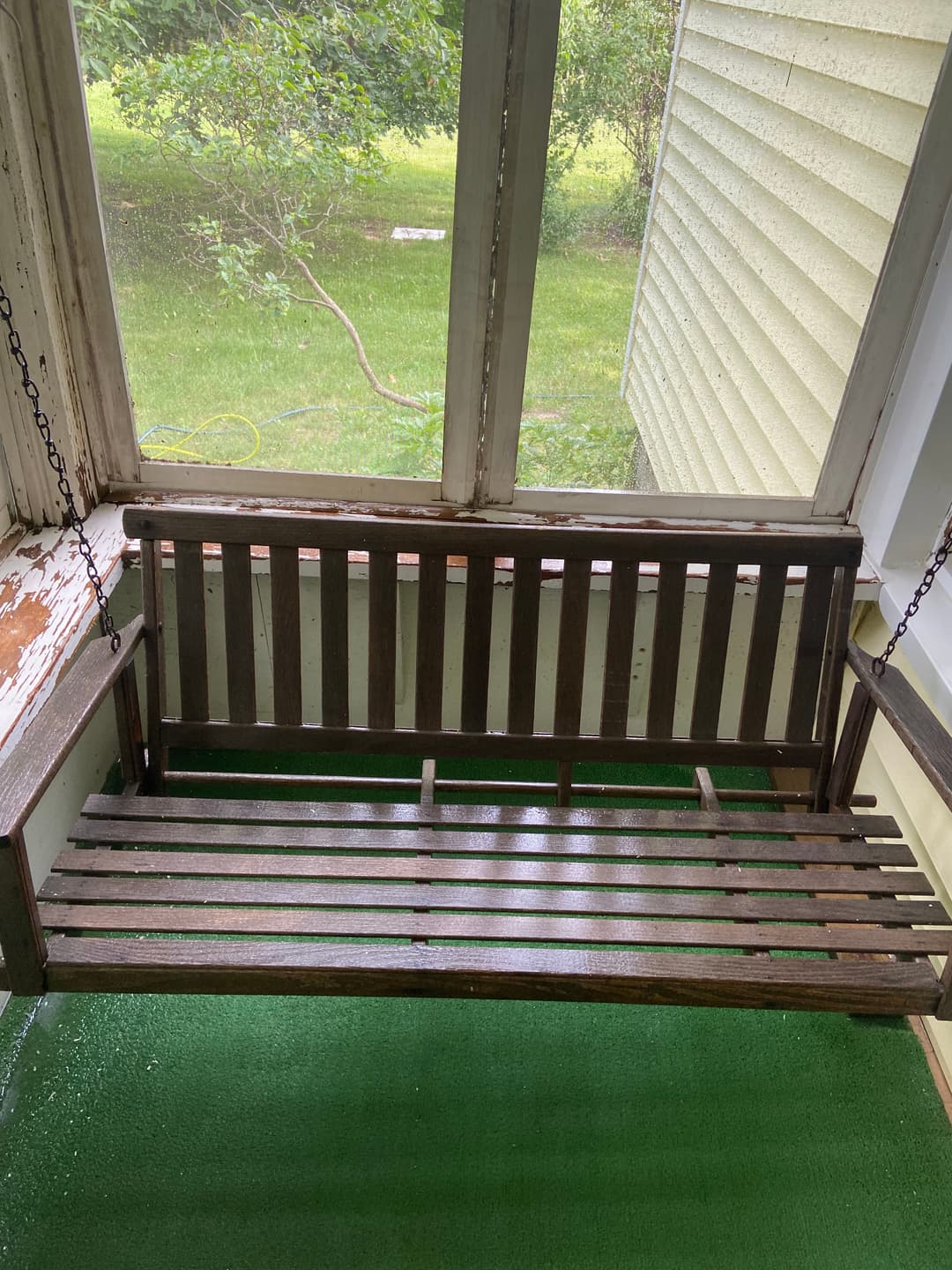 Rustic wooden porch swing in a screened-in area surrounded by greenery.