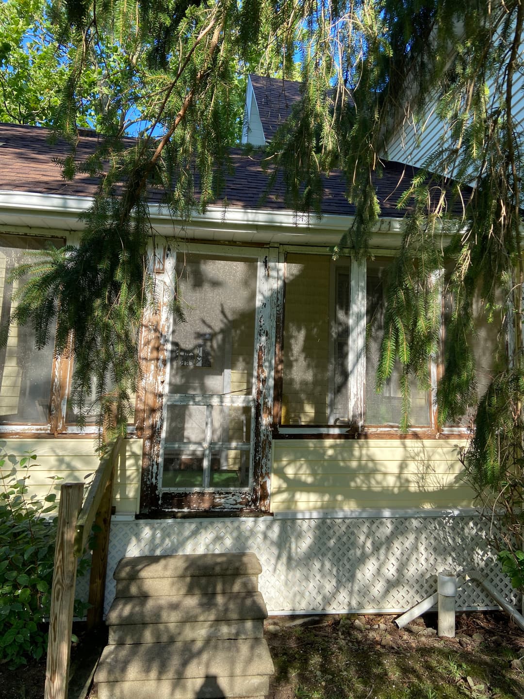 Old house with a screened porch surrounded by greenery and wooden steps.