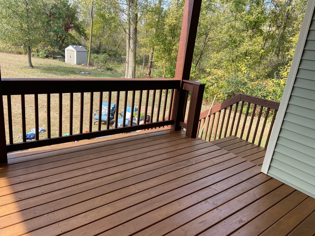 Wooden deck view overlooking a backyard with trees and a storage shed.